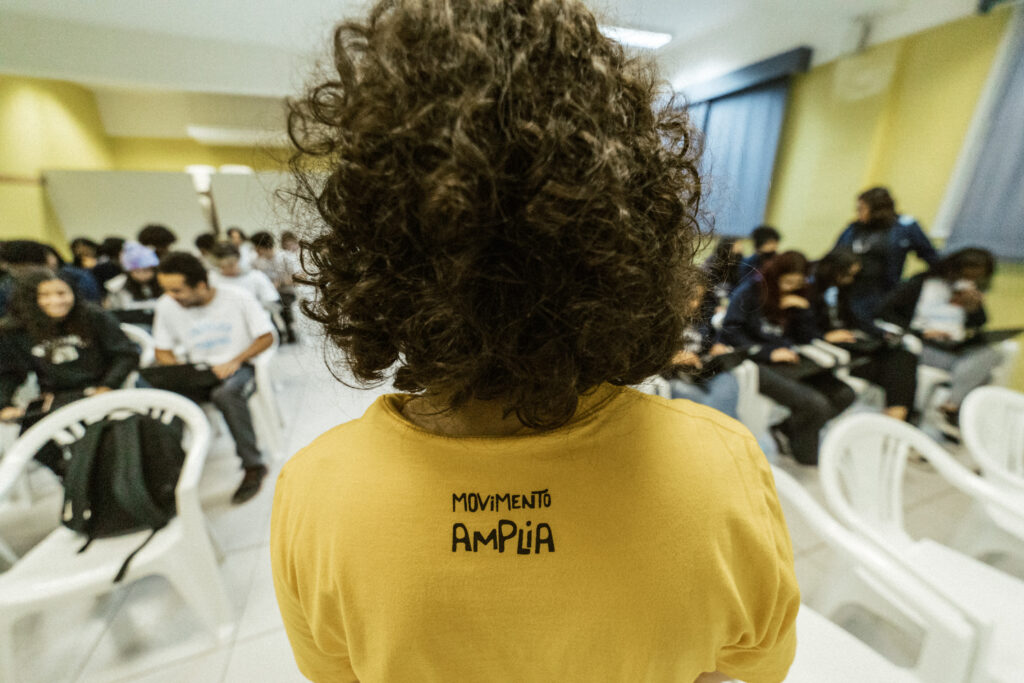 Imagem de menino vestido de camiseta amarela com logo do Movimento Amplia, de costas, cabelo cacheado.