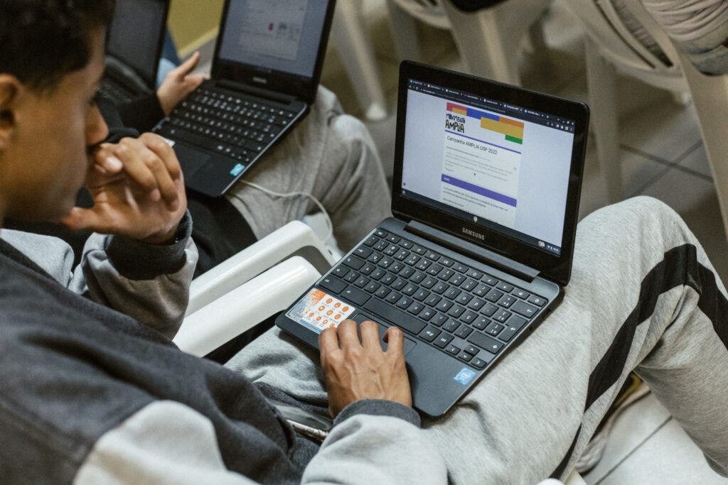 Foto de homem segurando notebook no colo, sentado, trabalhando.